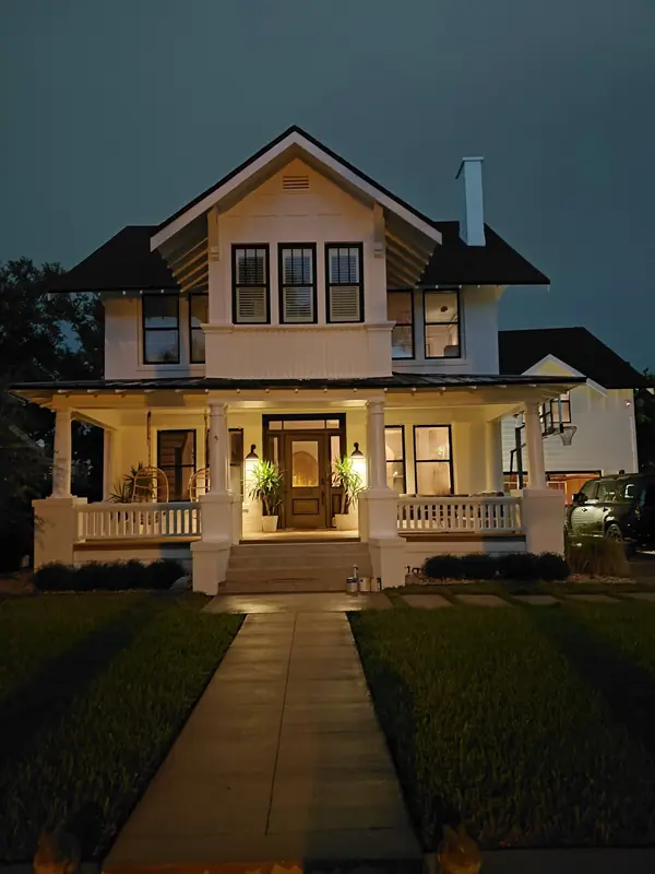 Two-story craftsman house at dusk with white siding, black window trim and a lit front porch