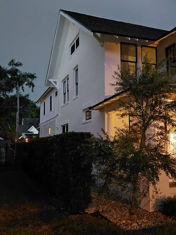 Side of a white two-story house with black-framed windows, lit at dusk