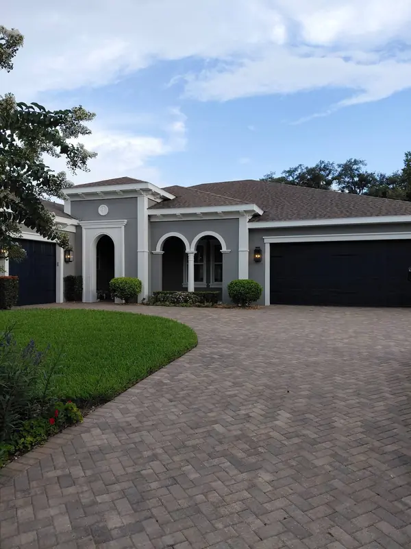 Single-story gray stucco home with white arched trim and a dark garage door