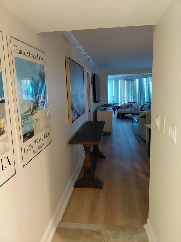 Long cream hallway with white baseboards leading to a sunny living room