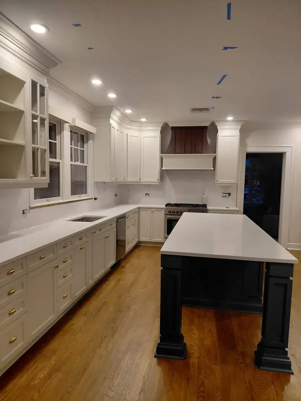 Long white kitchen with painted cabinets and a black island on wood floors