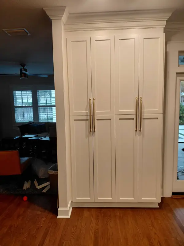Tall white pantry cabinets with brass handles and crown molding