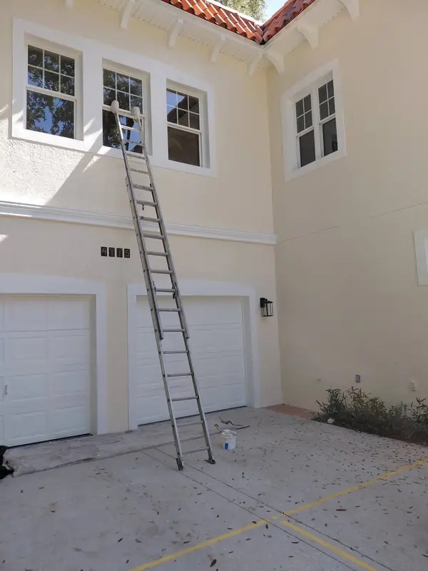 Ladder against a cream stucco wall above two white garage doors, mid-job